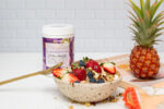 Mayella Acai Berry Blend sitting behoind a bowl filled with fresh fruits, granola and a smoothie bowl made with Mayella Acai Berry Blend. A pineapple sits on a wooden board to the right.