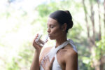 Beautiful woman drinking water in nature with hand on her heart.