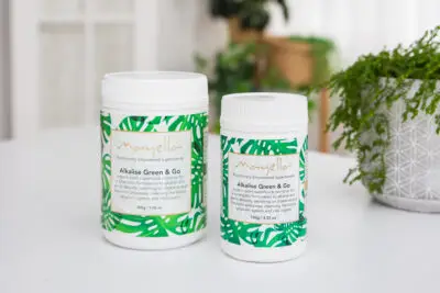 Mayella 100gm and 200gm size containers standing side by side on a white stone kitchen bench with a leafy green indoor plant to the right in the background.