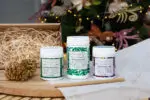 Mayella Organic Wheatgrass capsules, Acai Berry Beautiful Blend, Alkalise Green & Go Blend tubs standing together on a white table with fairy lights in the background suggesting a gift set purchase.