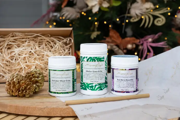 Mayella Organic Wheatgrass capsules, Acai Berry Beautiful Blend, Alkalise Green & Go Blend tubs standing together on a white table with fairy lights in the background suggesting a gift set purchase.