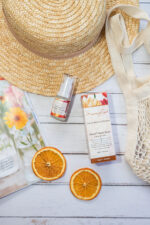 Mayella Olivane Citrus 15ml lies next to its box over the edge of a straw sunhat on a wooden deck with slices of orange and a folded magazine lying to the front.