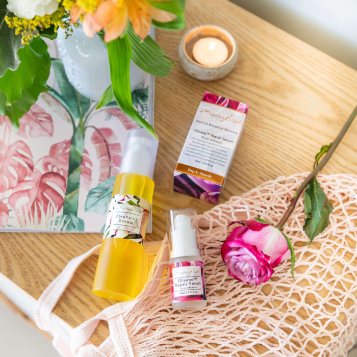 Mayella Cleansing Serum with Olivane Rose Serum lying across a string bag with a tea candle, pink rose and botanical magazine.