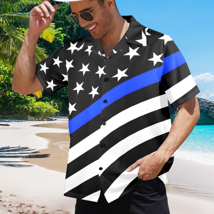 A man wearing a black button-up shirt with white stars and stripes, featuring a prominent blue line, standing on a beach.