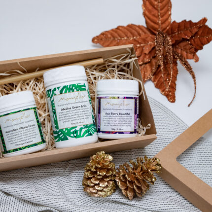 Mayella Nourish to Flourish set of three products sitting in a natural card box on straw with a bronze Christmas in background and two gold painted pine cones in front right corner.