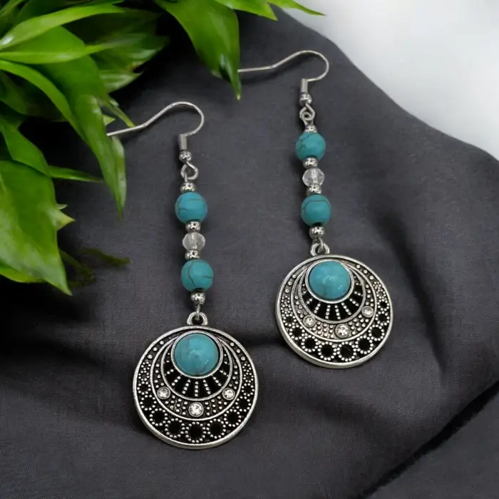 these stunning turquoise and silver tone earrings, featuring a unique circular design that perfectly captures the essence of boho style. Adorned with sparkling crystal beads, they add a touch of elegance and flair to any outfit, making them a must-have for your jewelry collection.