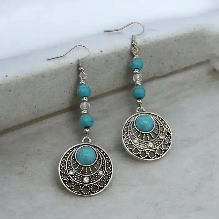 these stunning turquoise and silver tone earrings, featuring a unique circular design that perfectly captures the essence of boho style. Adorned with sparkling crystal beads, they add a touch of elegance and flair to any outfit, making them a must-have for your jewelry collection.