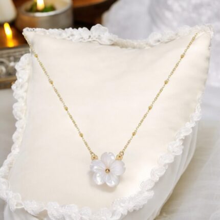 This exquisite necklace features a delicate white flower crafted from natural shell, elegantly suspended from a luxurious gold chain. The combination of the soft floral design and the shimmering gold creates a sophisticated accessory suitable for any occasion. Perfect for adding a touch of elegance to both casual and formal attire, this necklace is a timeless piece that enhances the beauty of the wearer.